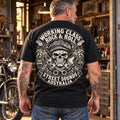 Man wearing the black Working Class Rock and Roll T-shirt in a motorcycle workshop, showing the skull crest back print