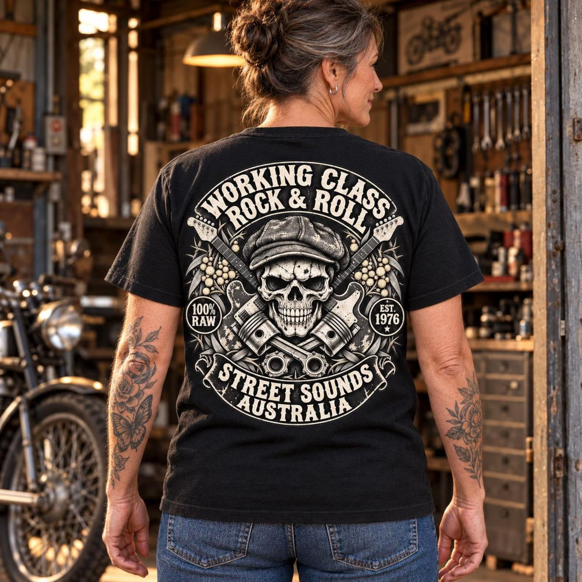 Woman wearing the black Working Class Rock and Roll T-shirt in a motorcycle workshop with the back print visible